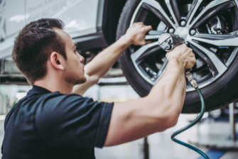 Handsome mechanic in uniform is working in auto service. Car repair and maintenance. Twisting/untwisting bolts on wheel.